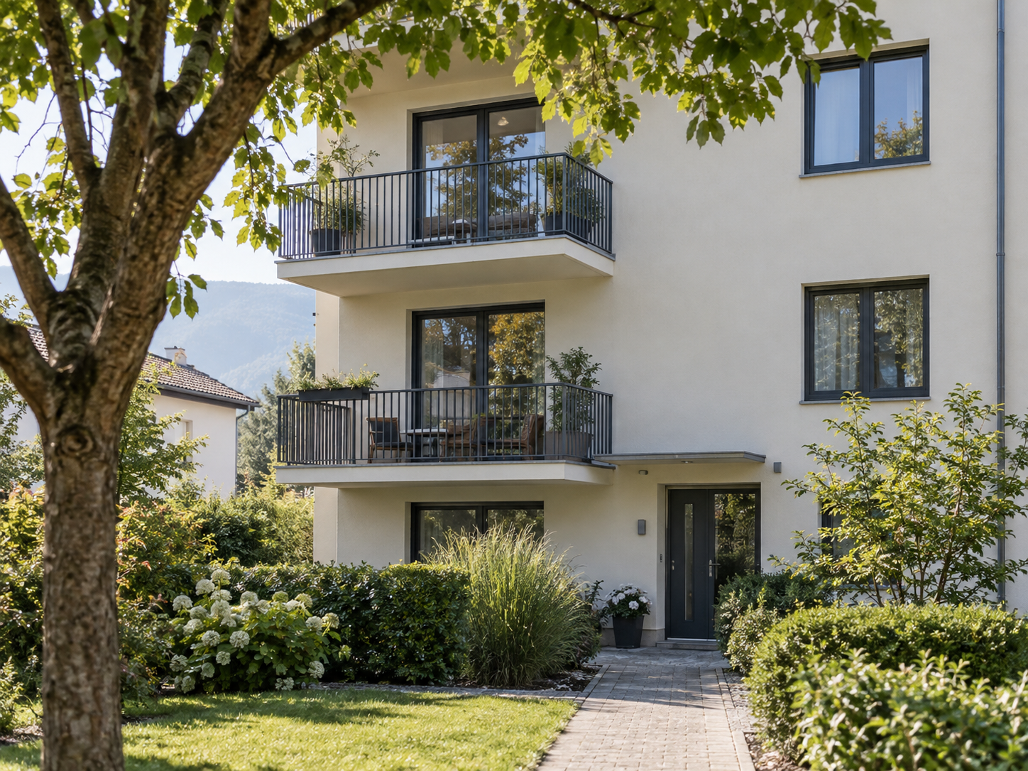 Wohnhaus mit zwei Balkonen und einem Baum vor der hellen Fassade