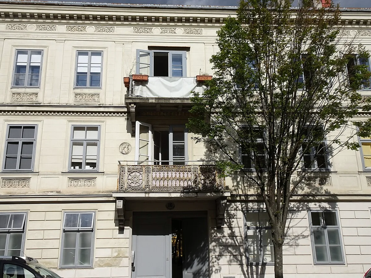 Österreichisches Wohnhaus mit mehreren Fenstern, Balkonen und einem Baum vor der Fassade